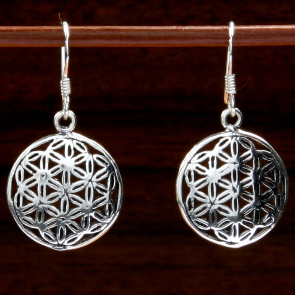 Two silver earrings featuring a seed of life design on a dark background