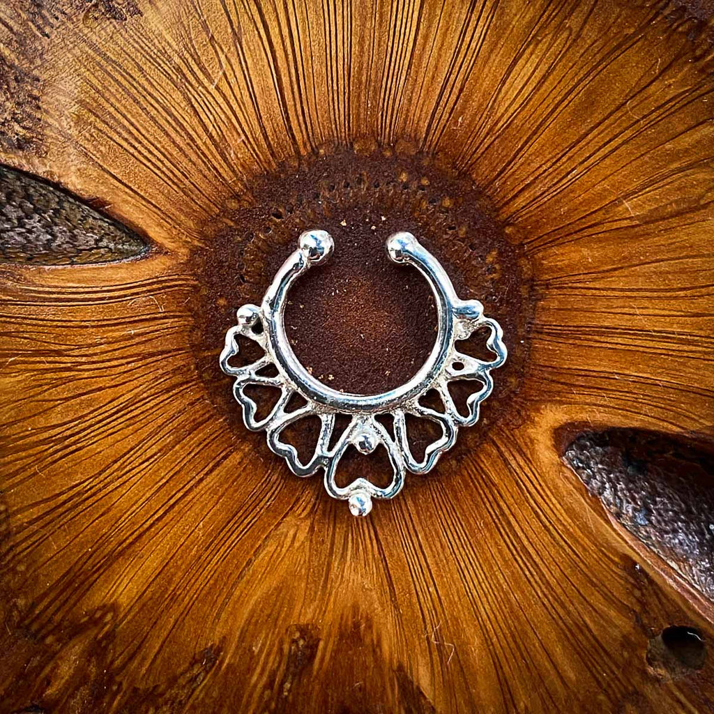 A fake silver septum jewel featuring a heart-inspired design on a wooden background