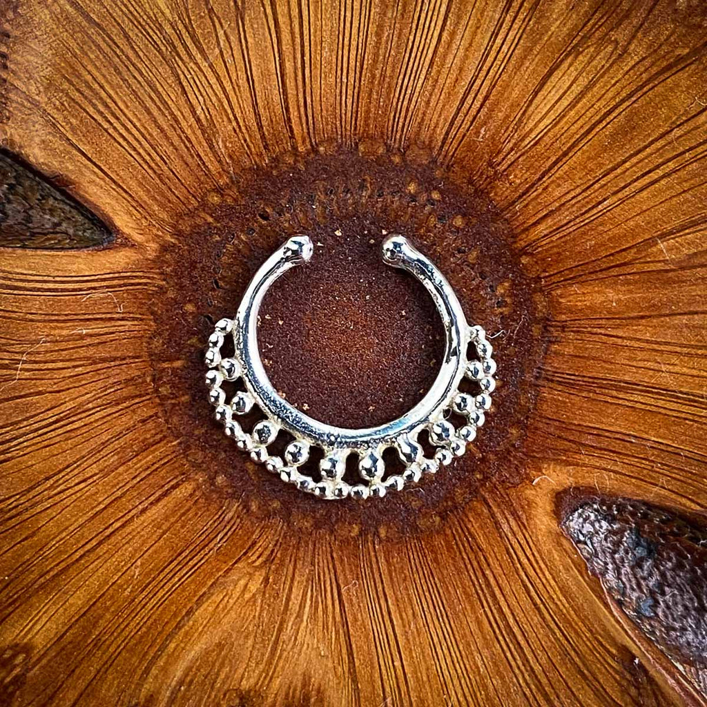 A fake septum jewel decorated with a belt of dots on a wooden background