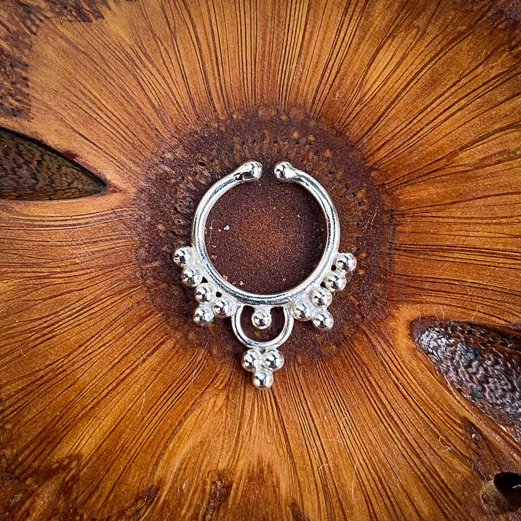 A silver fake septum jewel decorated with multiple dots on a wooden background