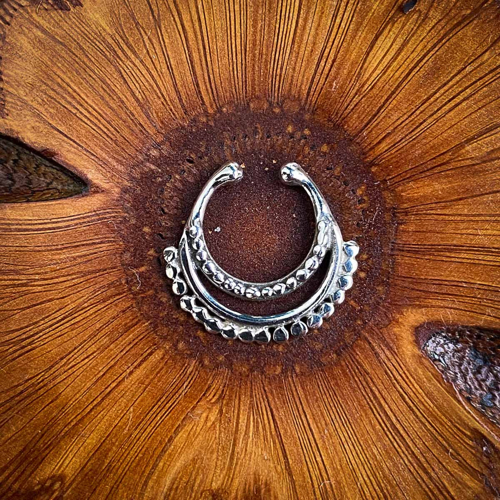 A fake silver septum jewel featuring a double dots belt on a wooden background