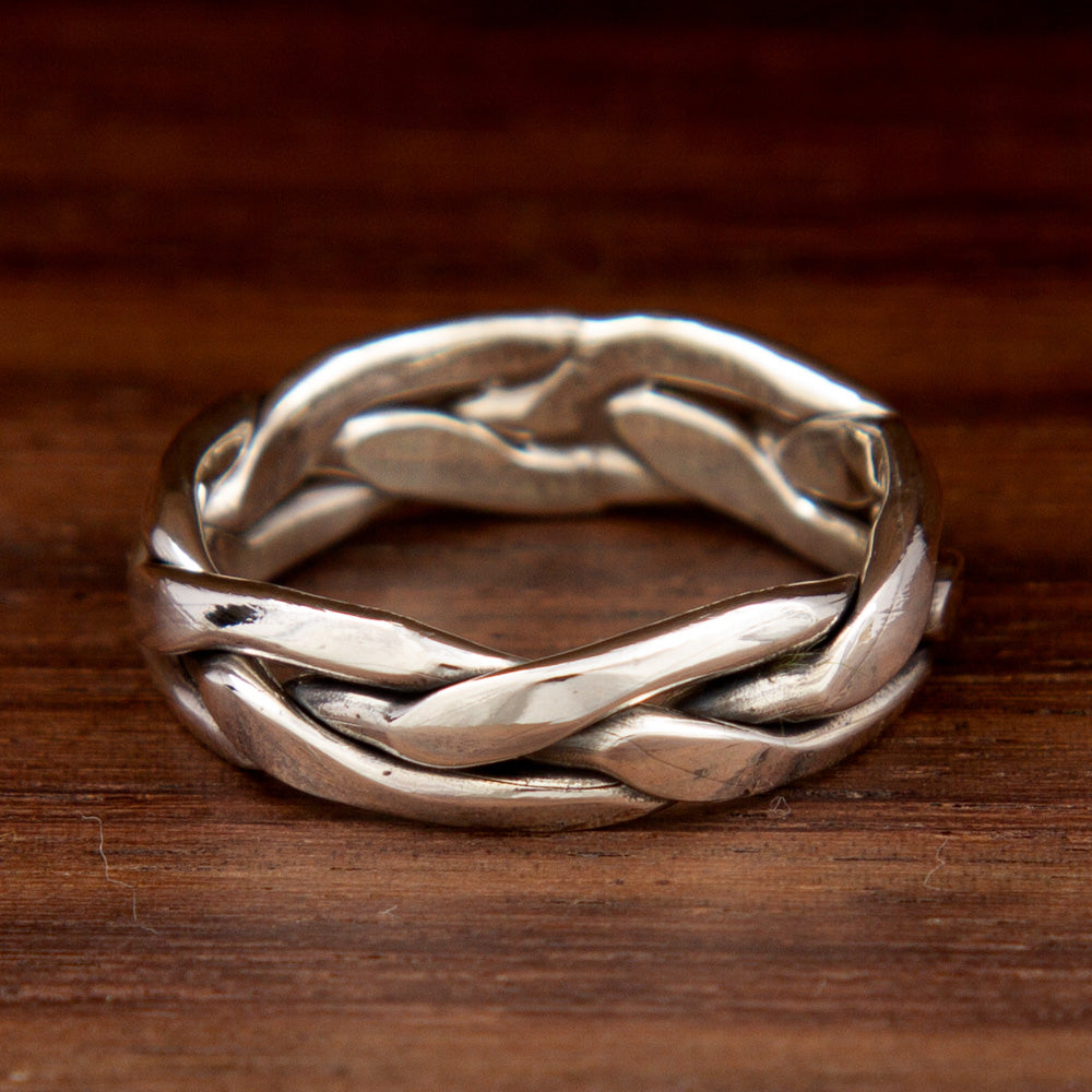 A silver ring featuring a plait design on a wooden background