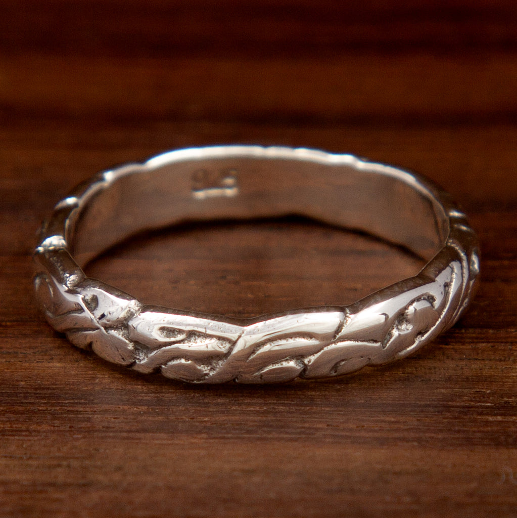 A silver ring featuring a swirl band design on a wooden background
