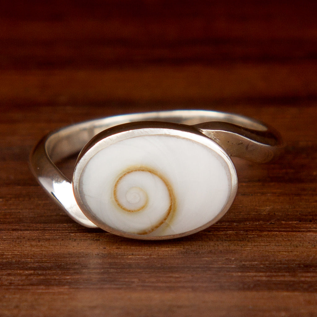 A silver ring featuring a white oval shell on a wooden background