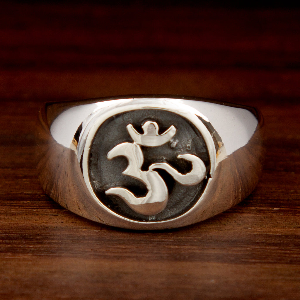 A silver band ring featuring the OM symbol on a wooden background