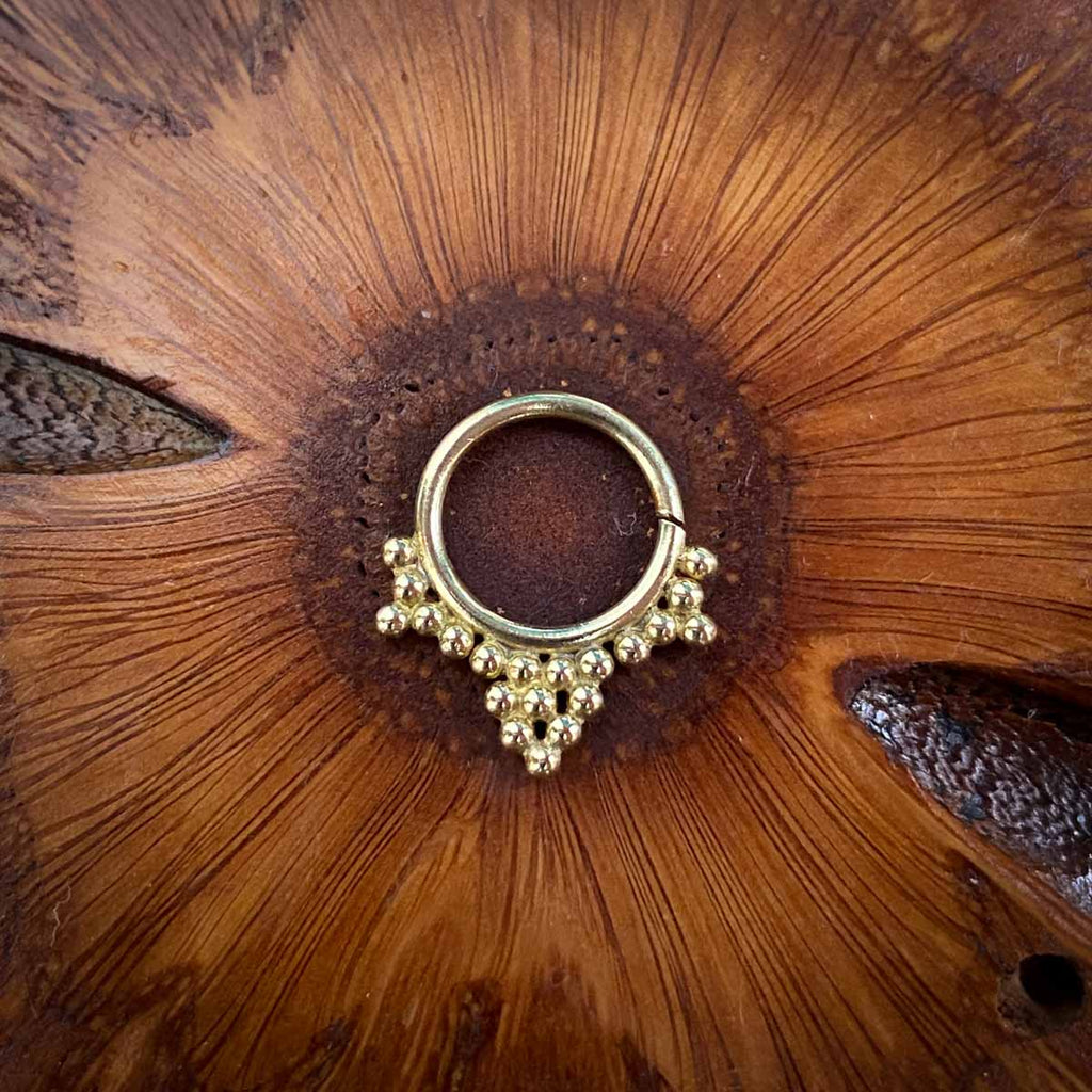 A Brass septum jewel decorated with multiple dots on a wooden background