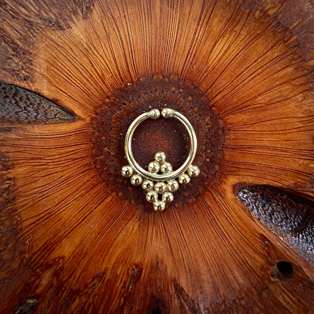 A Brass fake septum featuring a dotted design on a wooden background