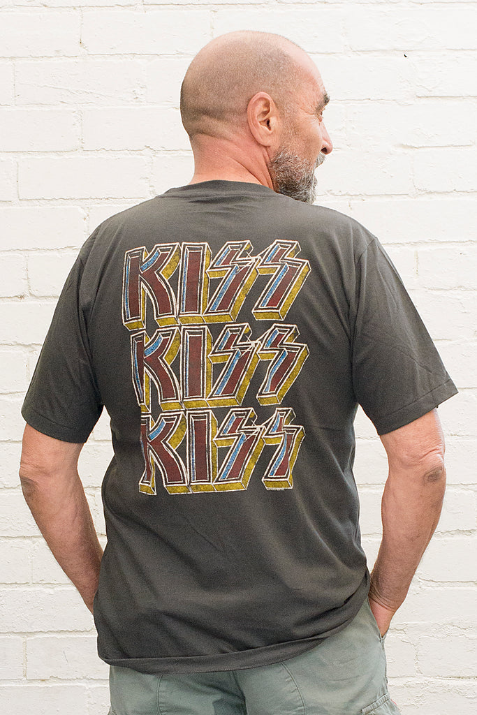 model wearing black cotton t-shirt with kiss logo repeated three times printed on back