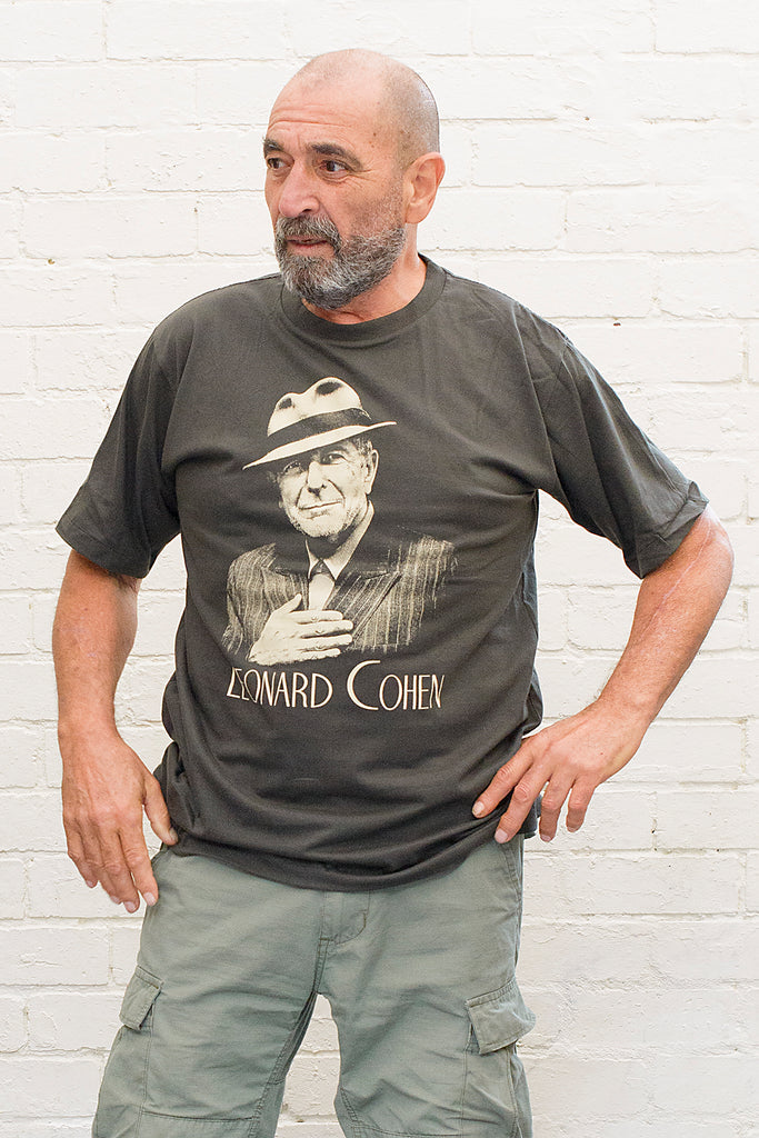 model wearing black cotton t-shirt with image of leonard cohen wearing hat and pinstripe suit with leonard cohen text printed below on front