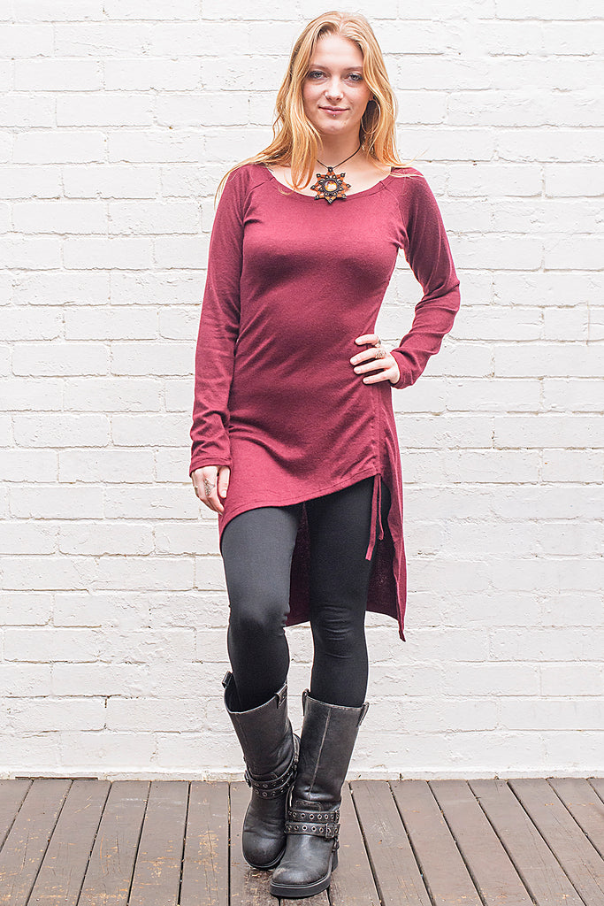 Model wearing a Khione knee length knit dress with boat collar and adjustable asymmetric hemline in maroon