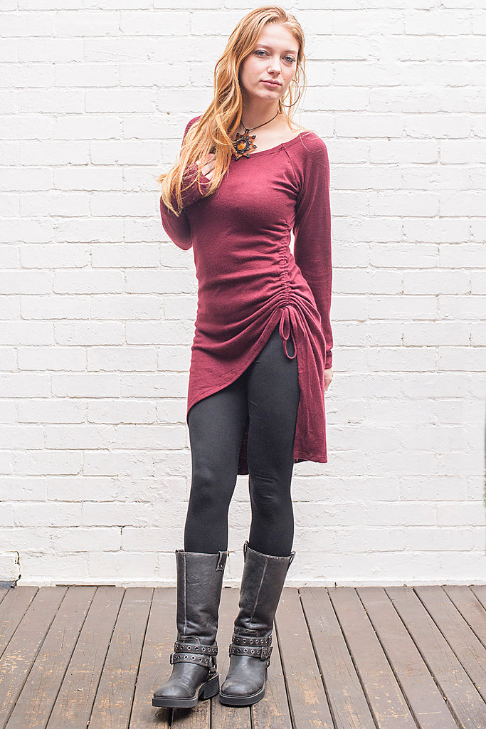 Model wearing a Khione knee length knit dress with boat collar and adjustable asymmetric hemline in maroon