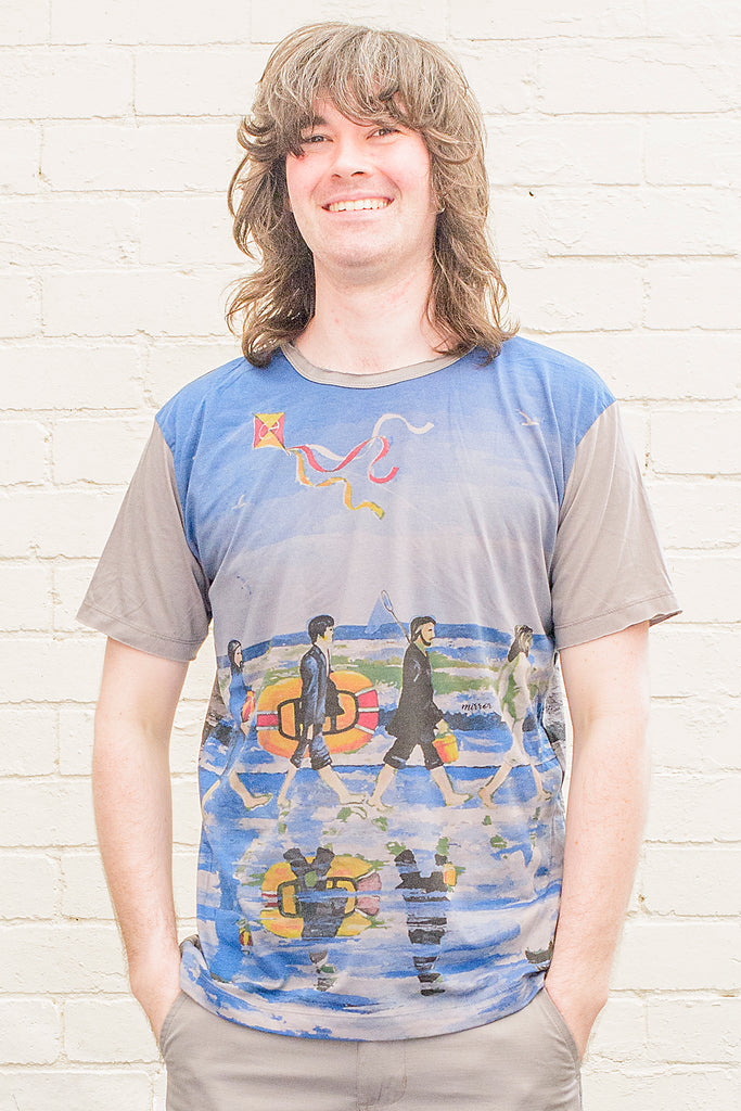 model wearing a grey T-shirt featuring a painterly design of the beatles walking along a beach with beach toys from the front