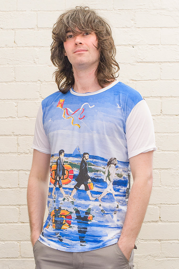 model wearing a white T-shirt featuring a painterly design of the beatles walking along a beach with beach toys from the front