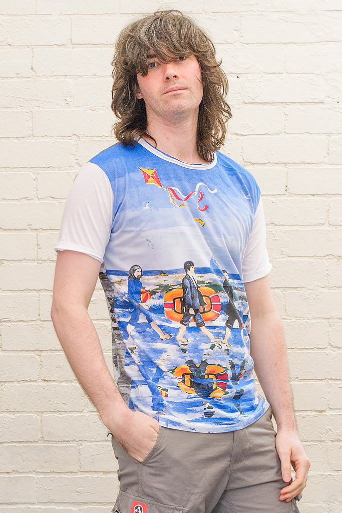 model wearing a white T-shirt featuring a painterly design of the beatles walking along a beach with beach toys from the front