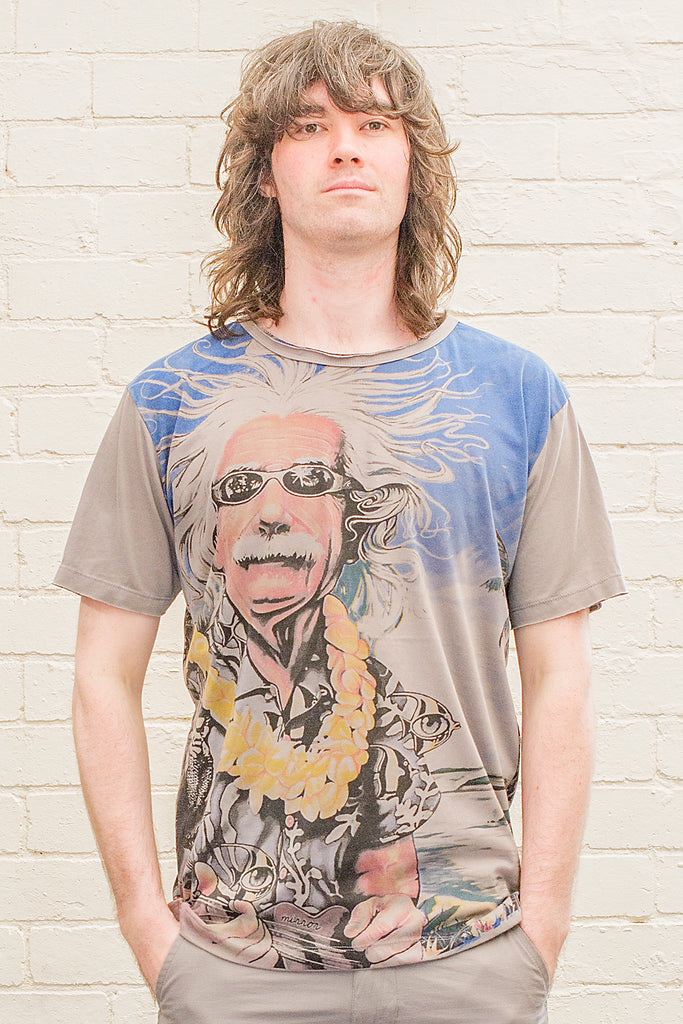 model wearing a grey T-shirt featuring a colourful caricature of albert einstein wearing sunglasses a hawaiian shirt and flower lei whilst playing ukelele at the beach printed on the front