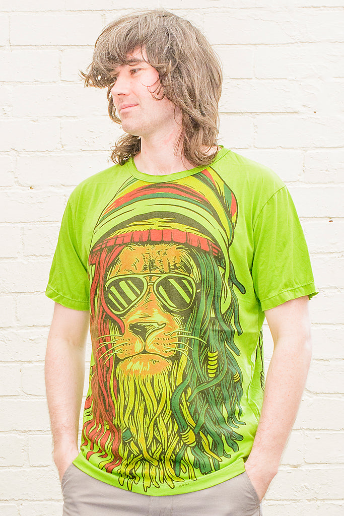 model wearing a bright green t-shirt printed with a cartoon image of the lion of judah with red gold and green dreadlocks and wearing sunglasses viewed from the front