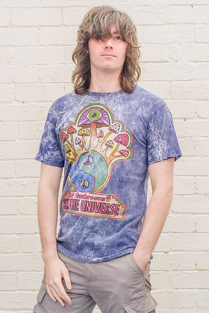 model wearing a blue stonewash t-shirt printed with a colourful magic mushroom graphic and eat mushrooms see the universe lettering from the front