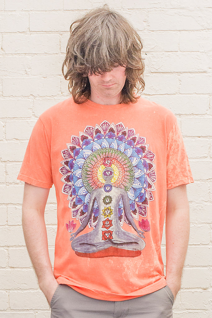 model wearing an orange stonewash t-shirt printed with an image of a yoga practitioner in lotus position with the 7 chakras illustrated and with a mandala behind the character viewed from the front