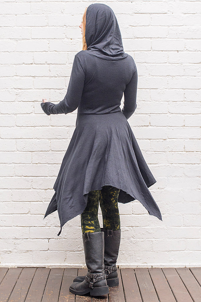 Model wearing a skadi midi length handkerchief hemline knit dress with hoodie and thumbholes in black from back