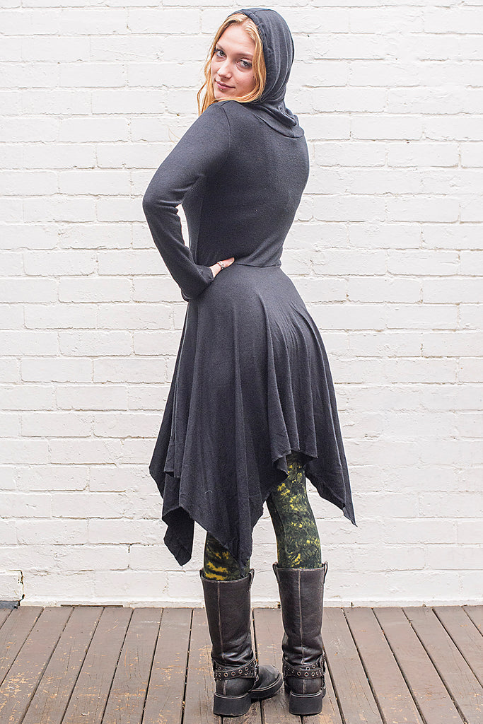 Model wearing a skadi midi length handkerchief hemline knit dress with hoodie and thumbholes in black from back