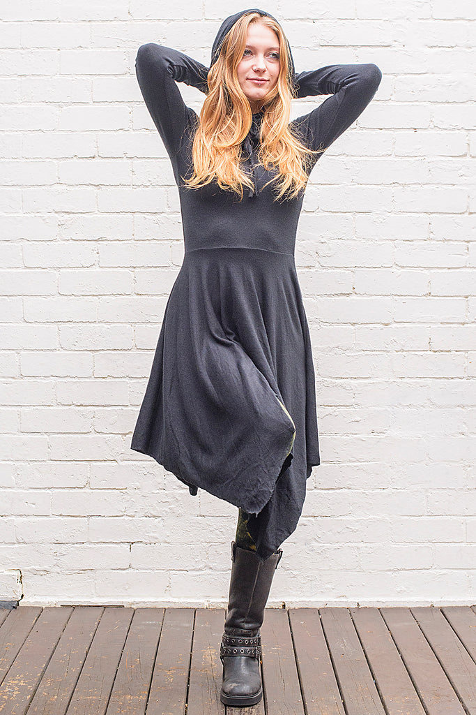 Model wearing a skadi midi length handkerchief hemline knit dress with hoodie and thumbholes in black