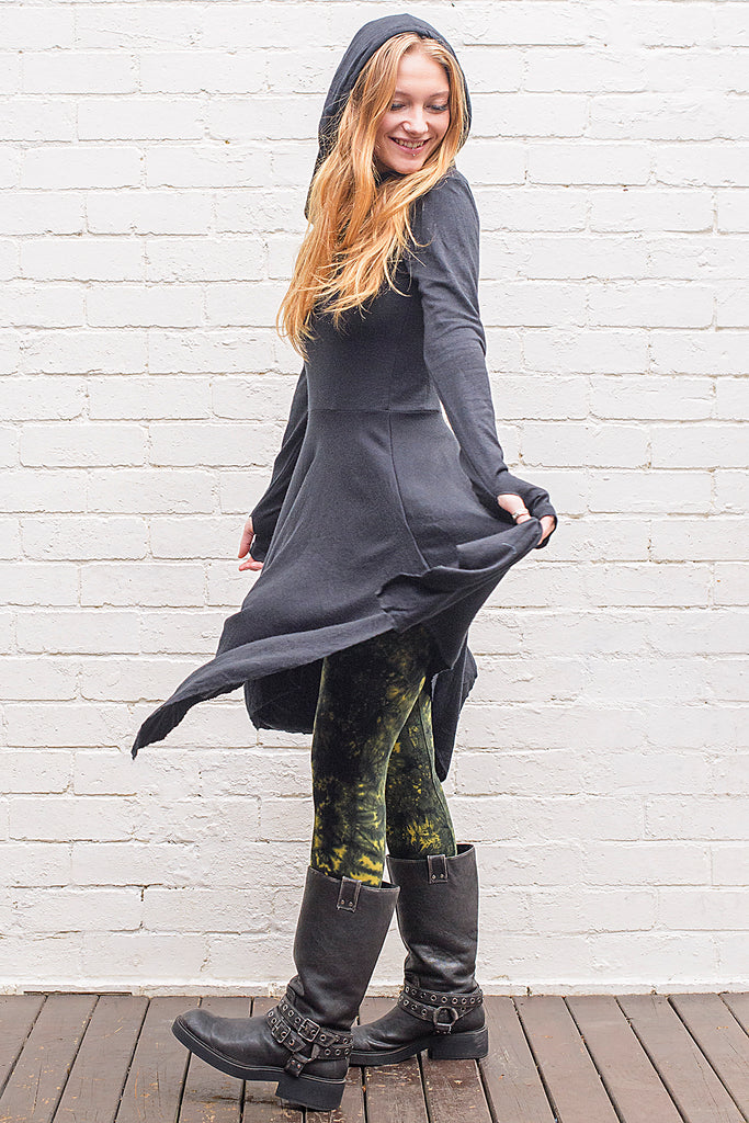 Model wearing a skadi midi length handkerchief hemline knit dress with hoodie and thumbholes in black from side