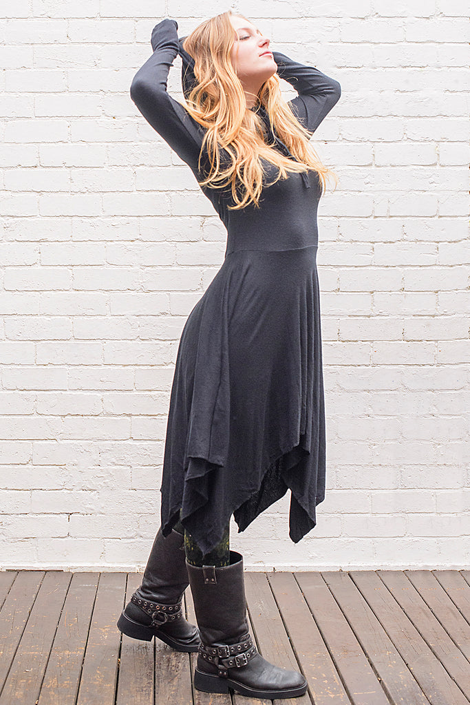 Model wearing a skadi midi length handkerchief hemline knit dress with hoodie and thumbholes in black from side