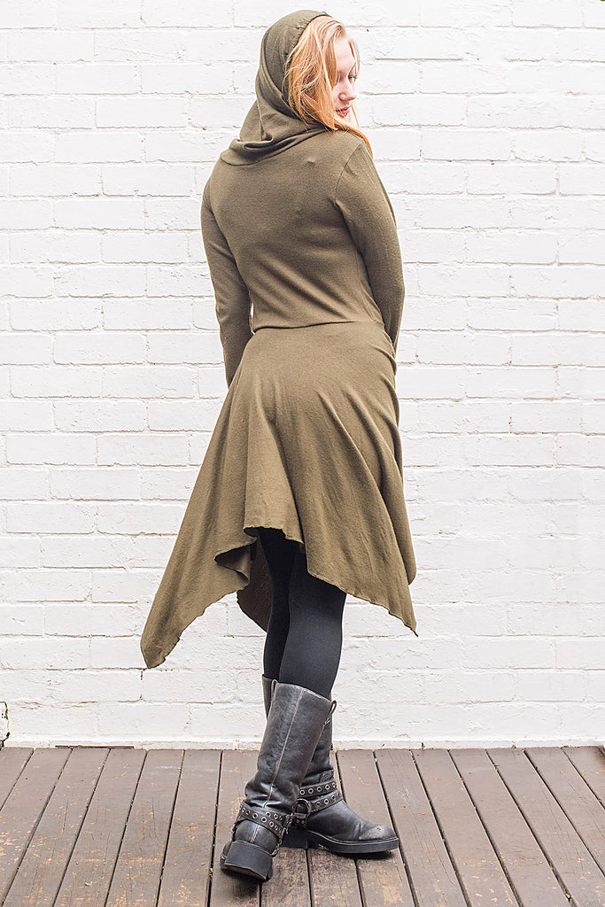 Model wearing a skadi midi length handkerchief hemline knit dress with hoodie and thumbholes in army green from back