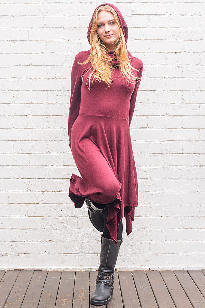 Model wearing a skadi midi length handkerchief hemline knit dress with hoodie and thumbholes in maroon