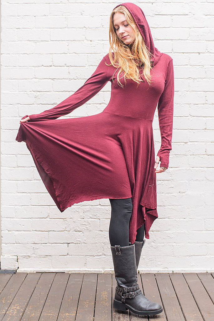 Model wearing a skadi midi length handkerchief hemline knit dress with hoodie and thumbholes in maroon