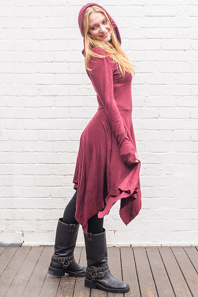 Model wearing a skadi midi length handkerchief hemline knit dress with hoodie and thumbholes in maroon from side