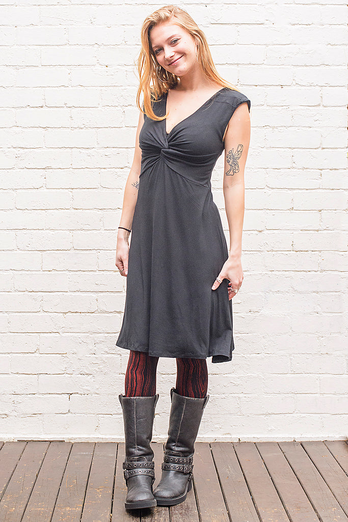 Model wearing v neck knee length dress with a twist at front and back in black from front