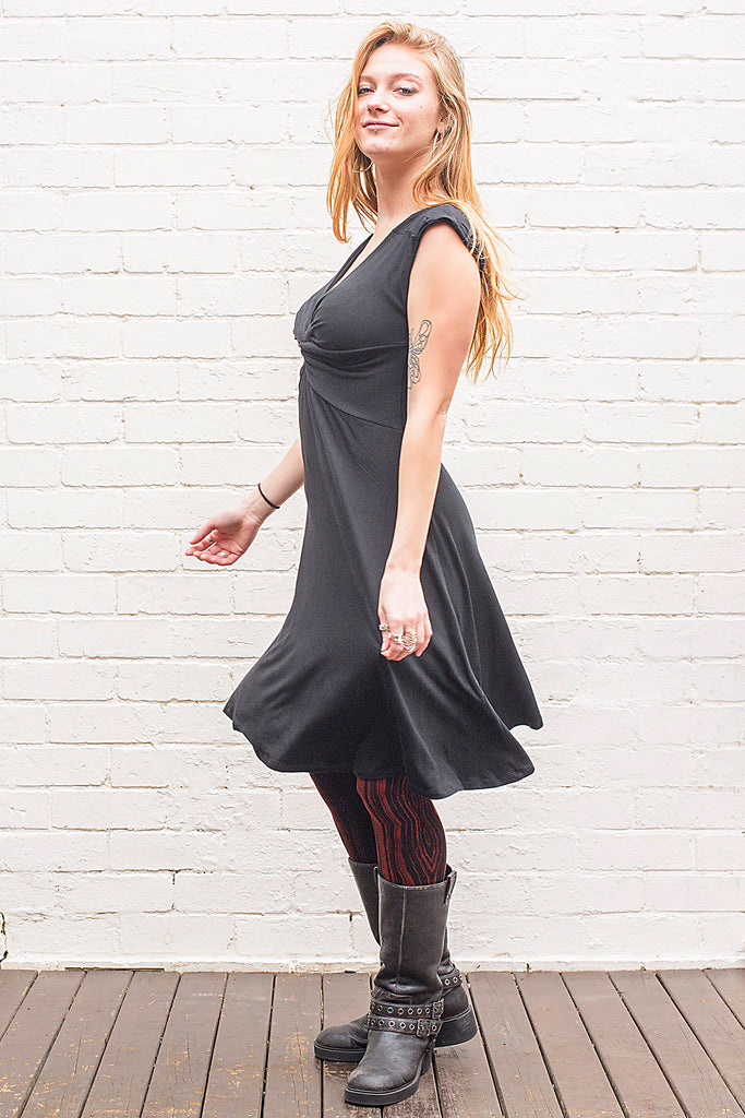 Model wearing v neck knee length dress with a twist at front and back in black from side