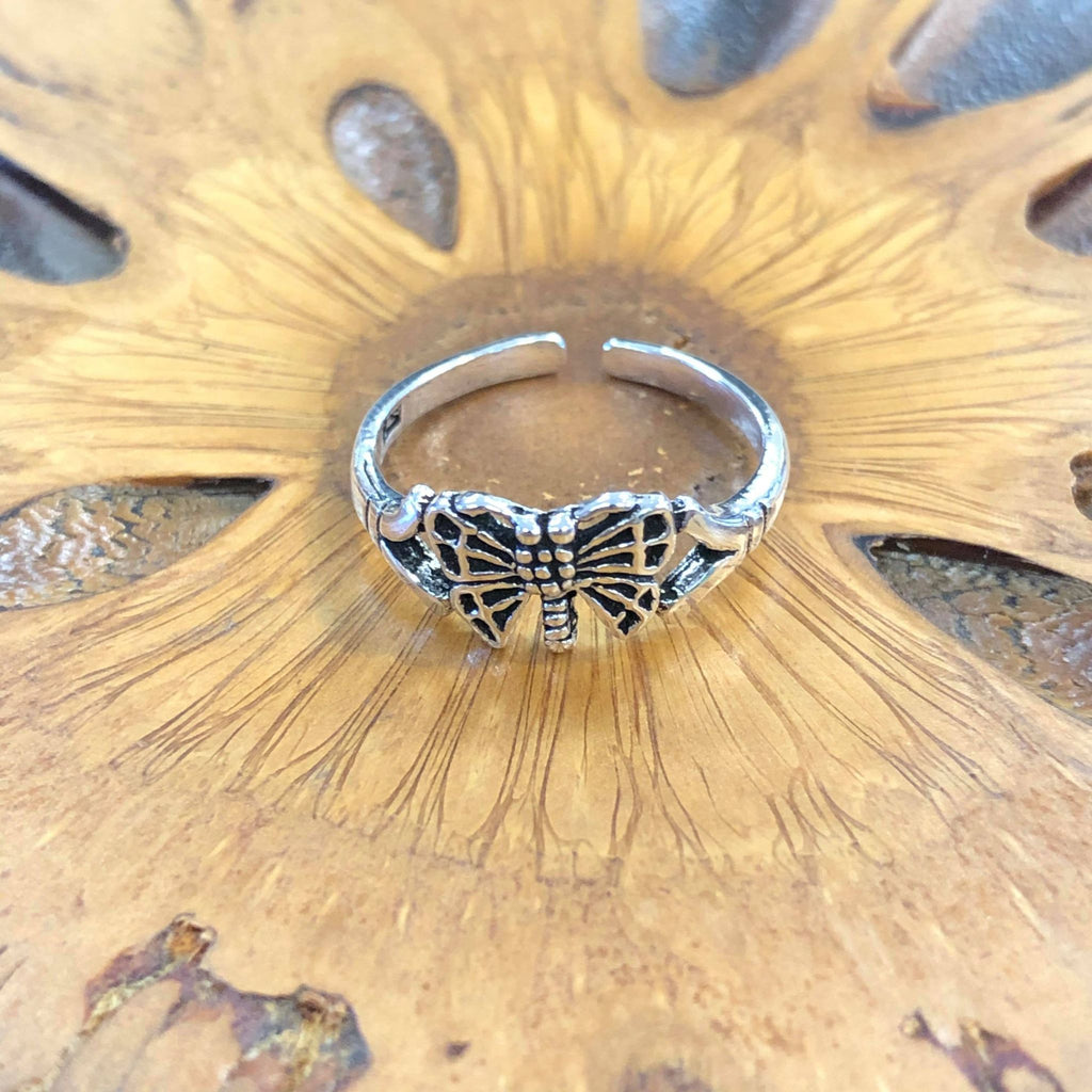 A silver toe ring featuring a butterfly design on a wooden background