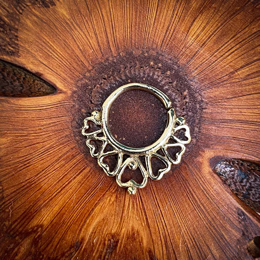 A brass septum jewel decorated with hearts on a wooden background