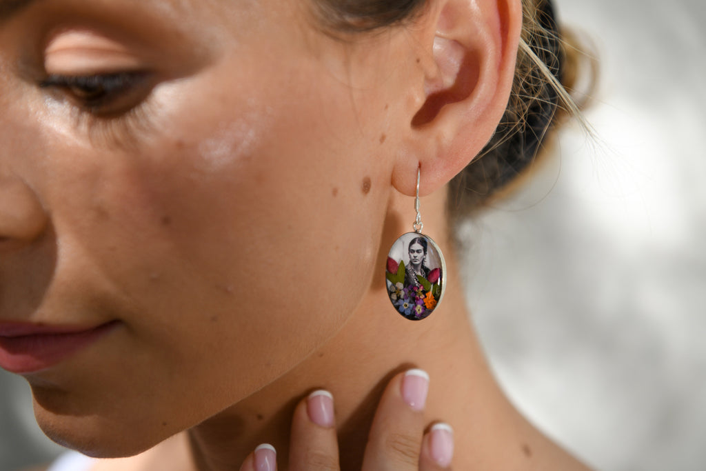 model wearing san marco silver and resin pendant earring featuring a photograph of frida kahlo adorned with colourful dried flowers