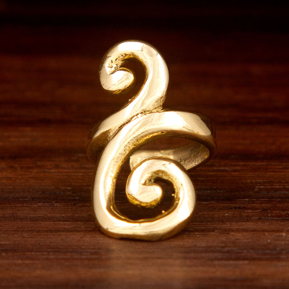 A brass ear cuff feraturing a spiral design on a wooden background