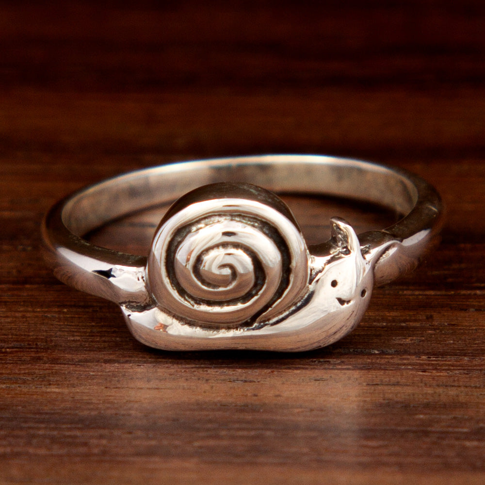 A silver ring featuring a snail design on a wooden background