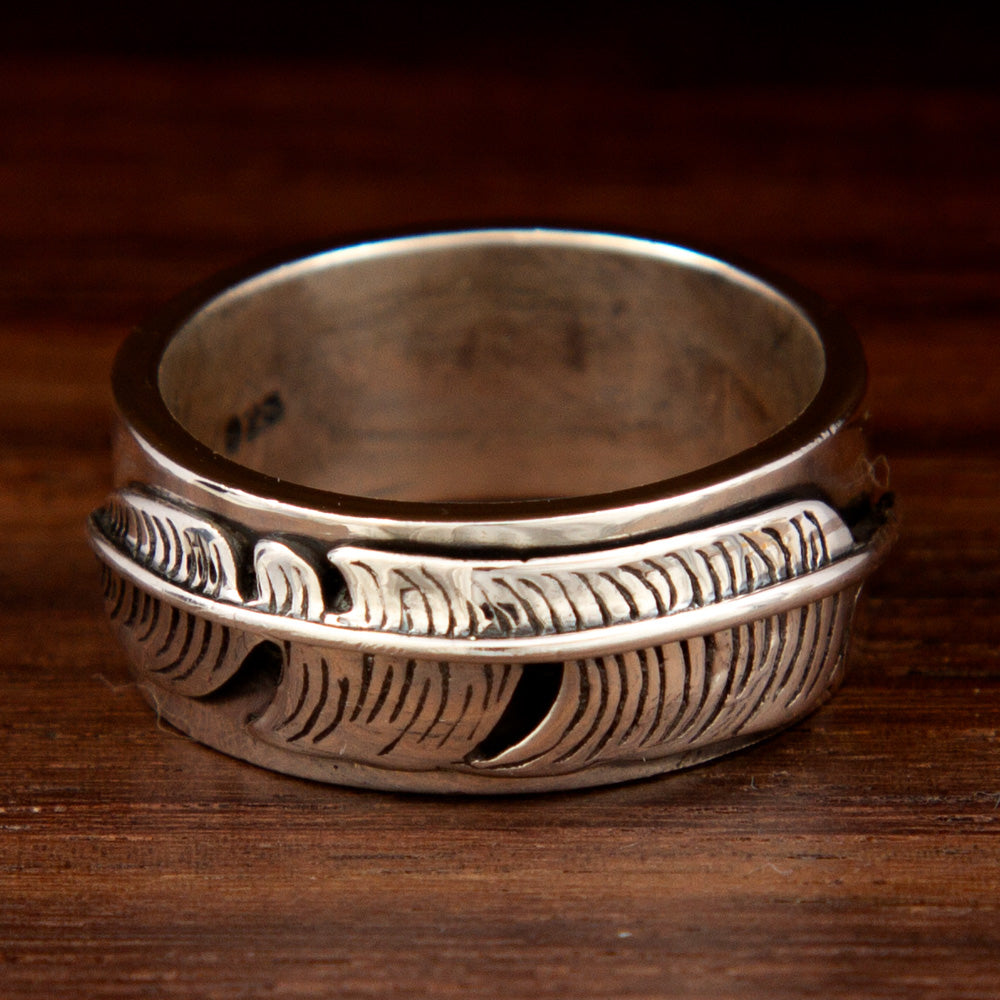 A silver thick ring featuring a feather band design on a wooden background