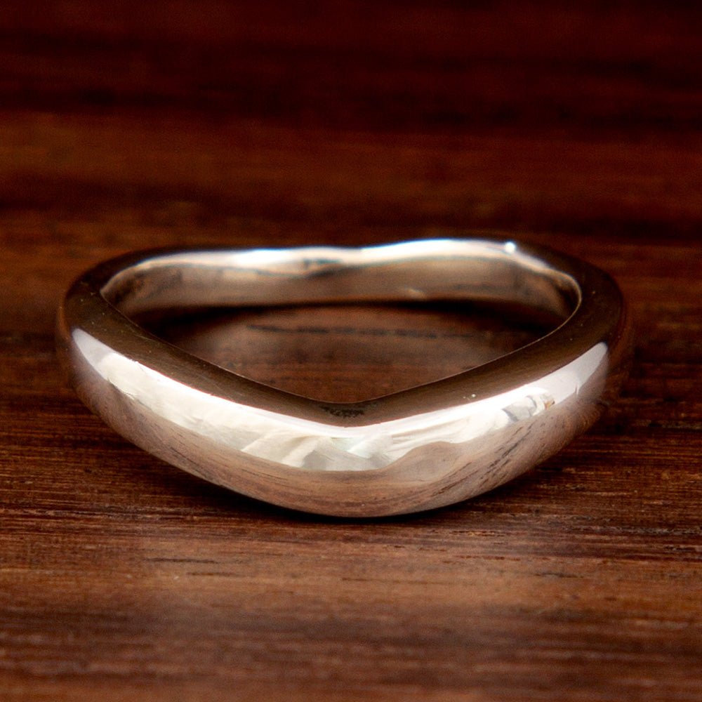 A sterling silver mid-finger ring featuring a bent design on a wooden background