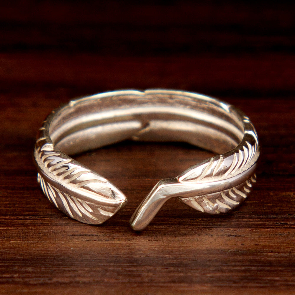 A silver mid-finger ring featuring a leaf design on a wooden background