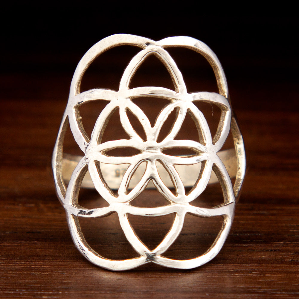 Sterling silver ring showcasing a thin band and a large flower of life design on a wooden background
