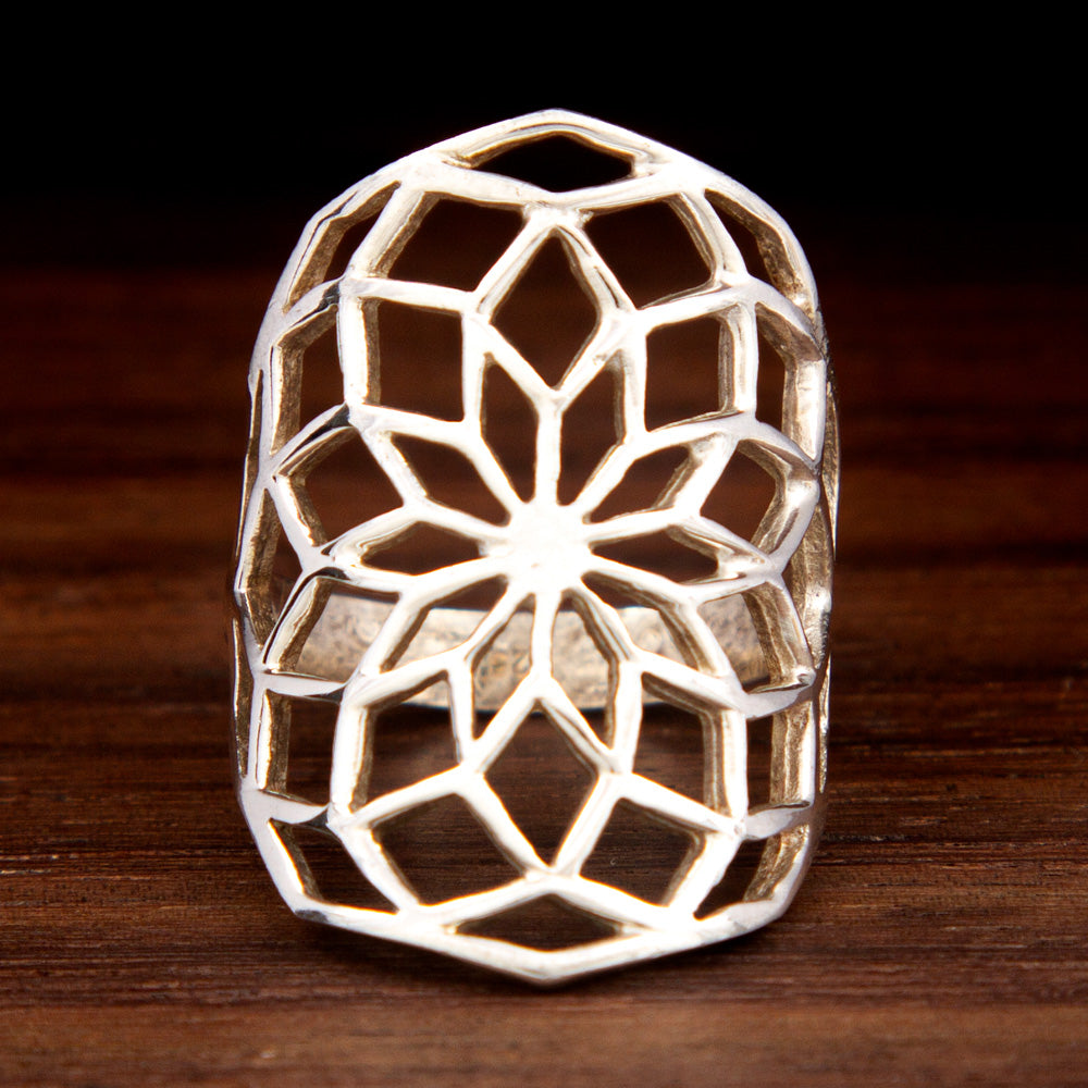 A silver ring featuring a sacred geometry design on a wooden background