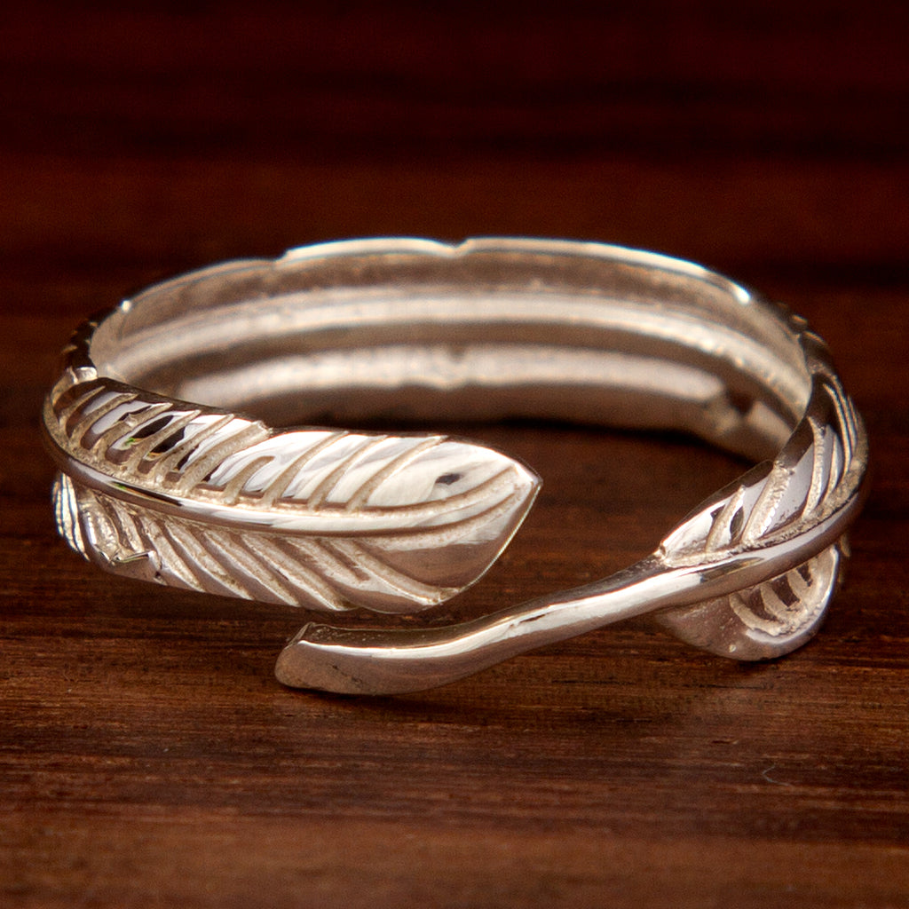 A silver adjustable ring featuring a leaf band design on a wooden background