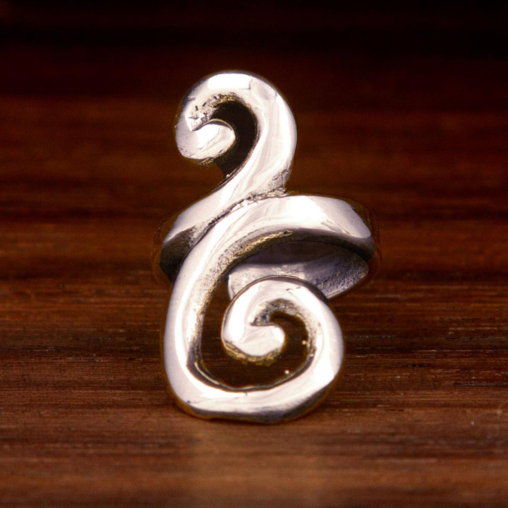 A silver ear cuff feraturing a spiral design on a wooden background