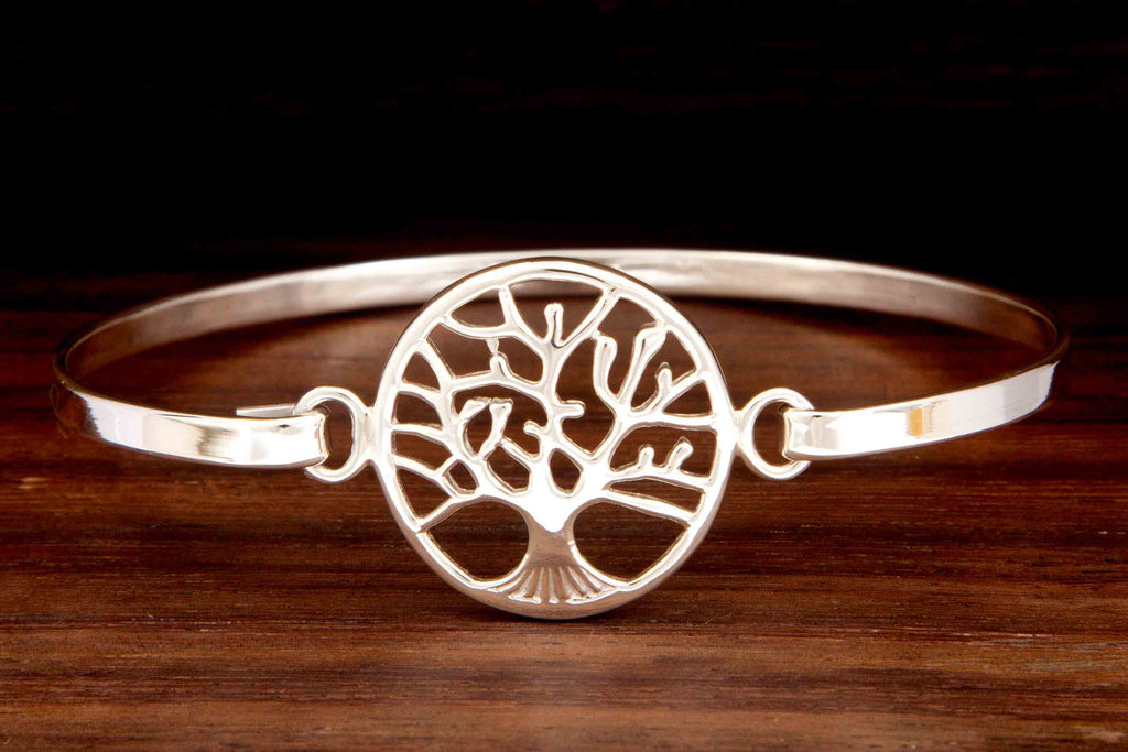 A silver cuff featuring a circled tree of life design on a wooden background