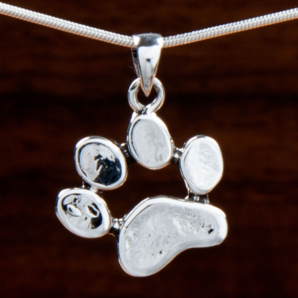 A sterling silver pendant featuring a paw print design on a wooden background
