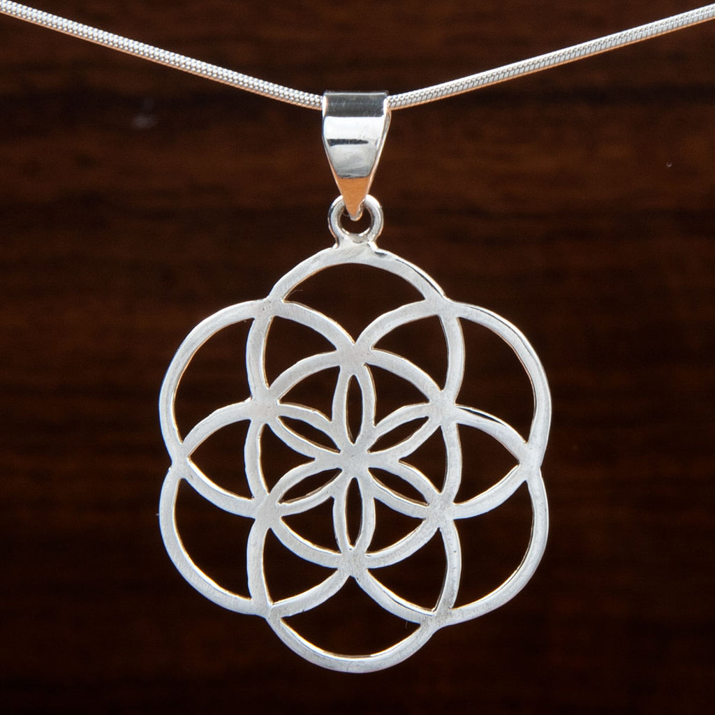 A silver pendant featuring a flower of life design on a wooden background