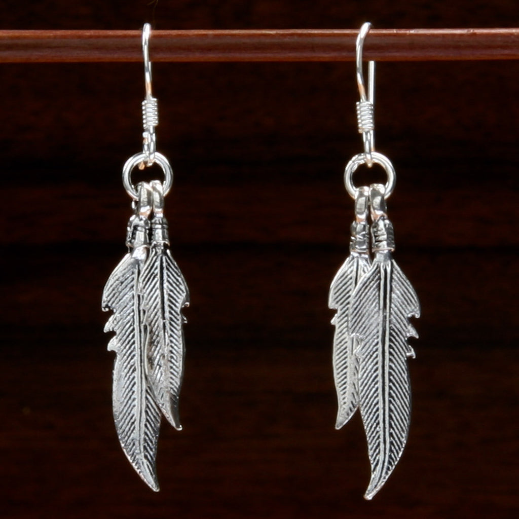 Two sterling silver earrings showcasing a feather design on a wooden background