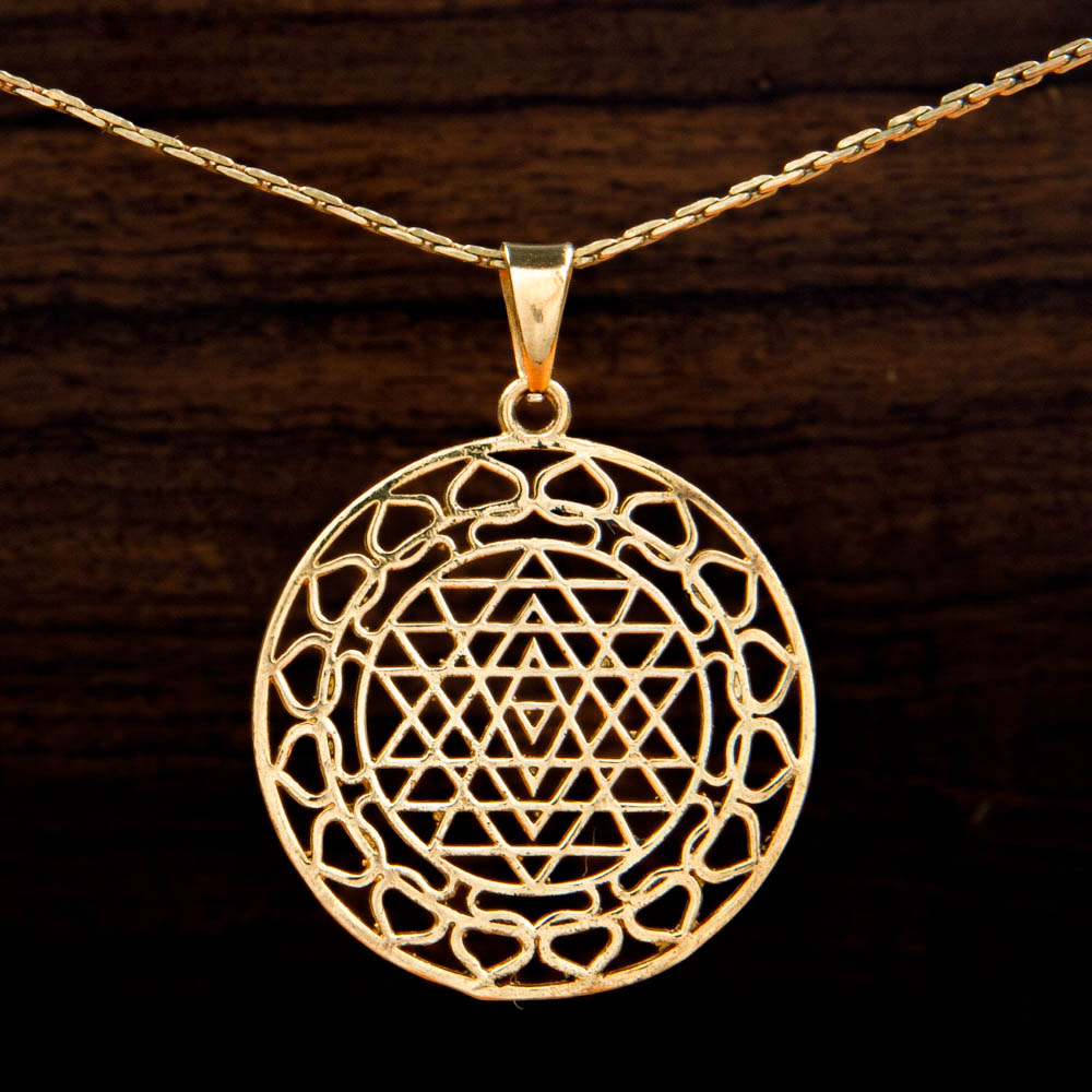 A brass pendant featuring a Sri Yantra design on a wooden background